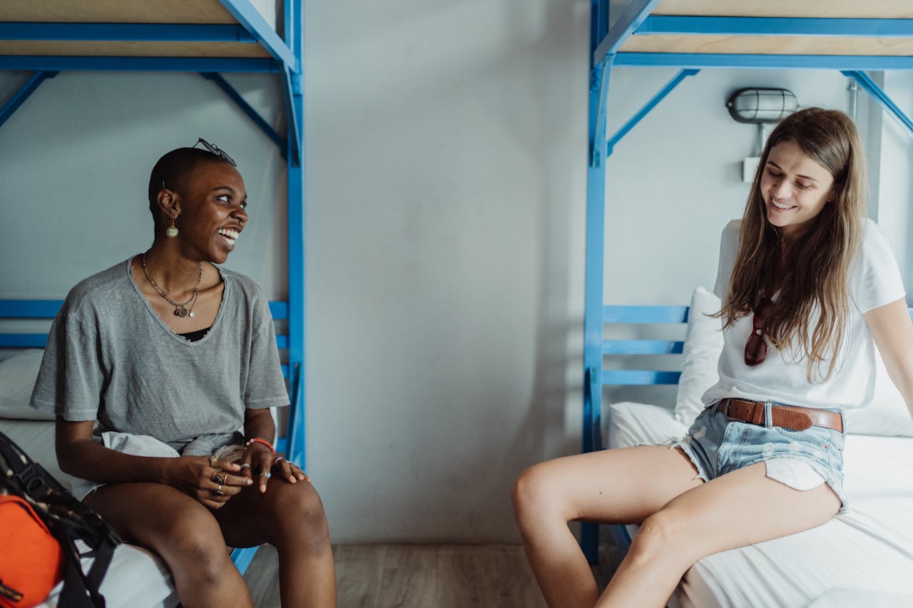 Two women chatting and smiling in a hostel room with bunk beds.