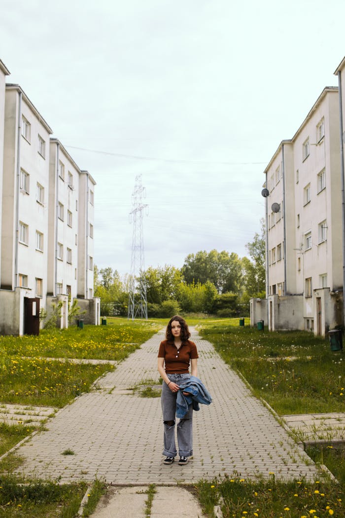 A woman standing on a paved path between two residential buildings.
